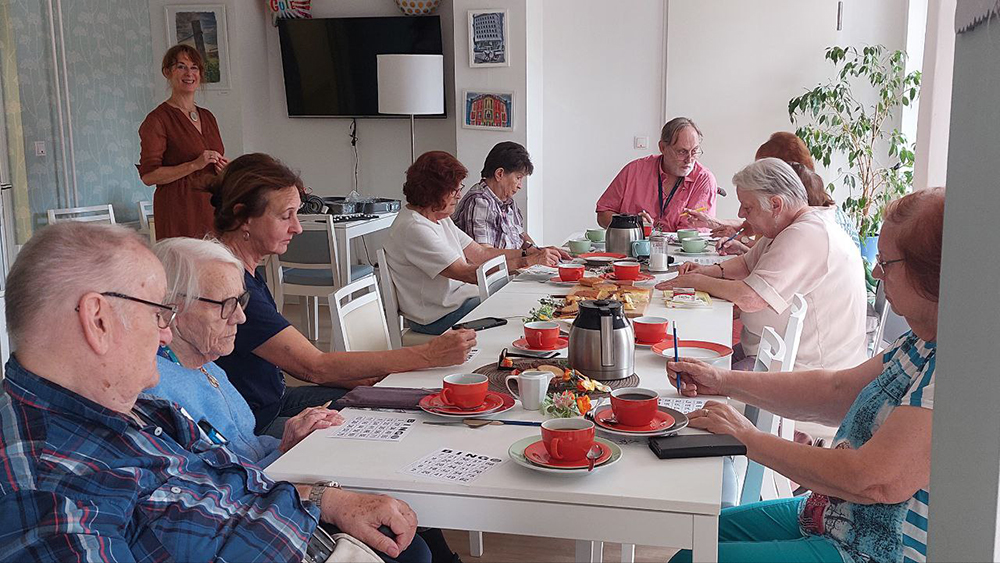 Neun Erwachsene sitzen an einem Tisch und spielen Bingo