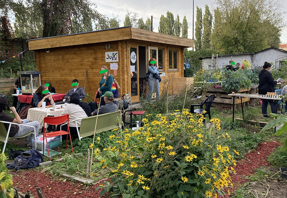 Foto des Gemeinschaftsgartens JuX mit Häuschen, Tisch, Besucherinnen und Pflanzen